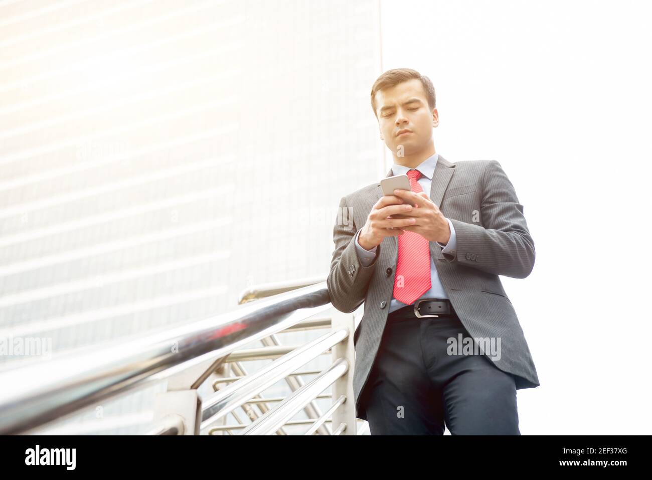 Uomo d'affari che usa lo smartphone mentre cammina sul ponte pedonale nel città Foto Stock