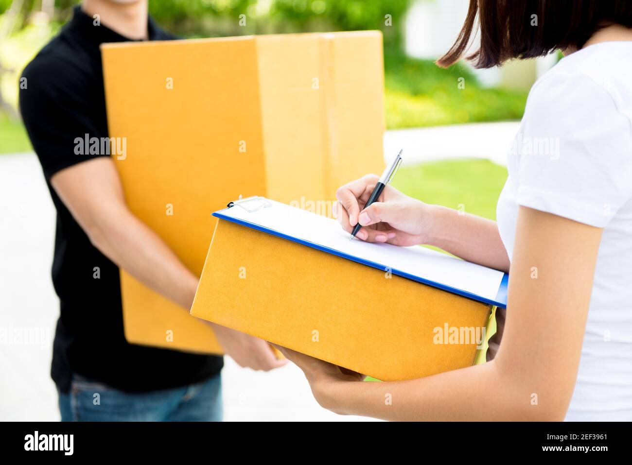 Donna che firma il documento, che riceve la scatola del pacco da uomo di consegna - concetto di servizio di corriere Foto Stock