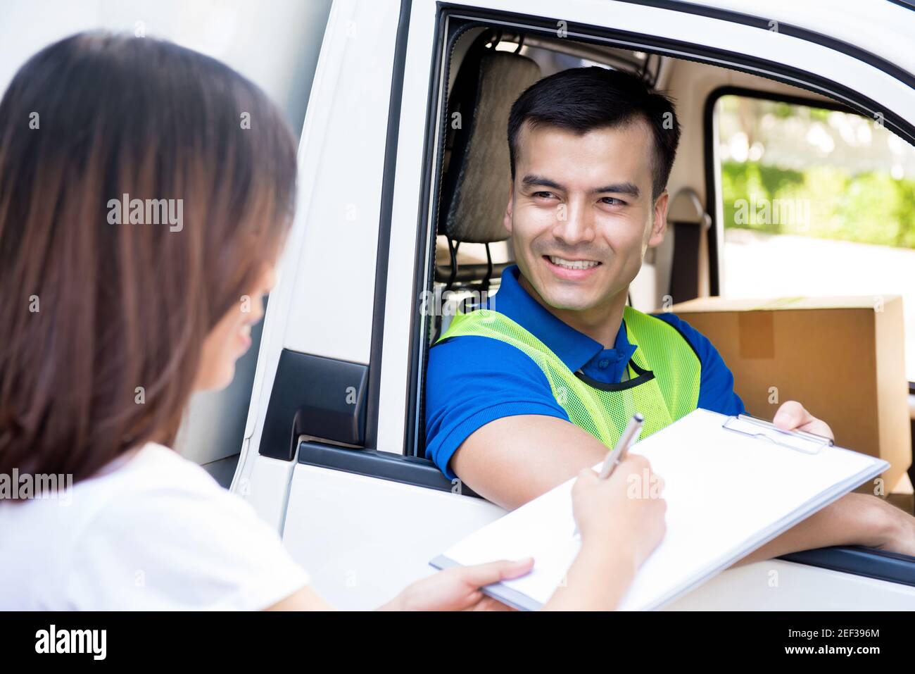 Consegna uomo in macchina consegna pacco a una donna e dando il suo documento da firmare Foto Stock