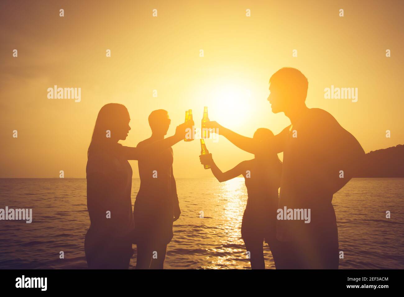 Silhouette di persone che hanno festa, bottiglie di birra claging, fare un brindisi alla spiaggia al tramonto Foto Stock