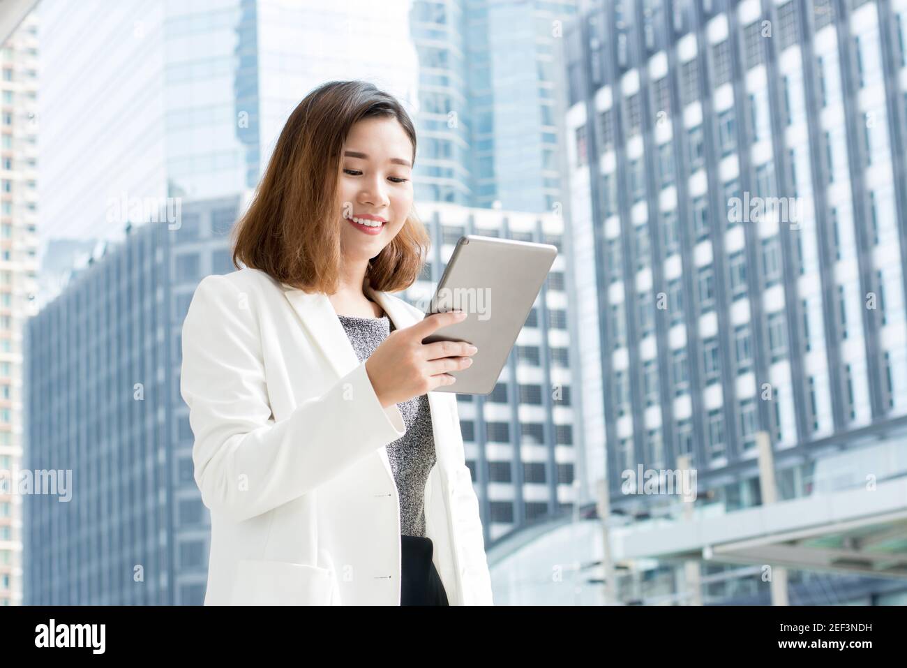 Donna d'affari asiatica che usa il computer tablet all'aperto nell'edificio offuscato dell'ufficio sfondo della città Foto Stock