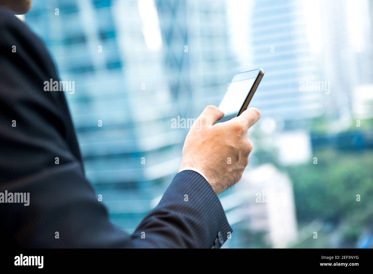 Uomo d'affari che usa lo smartphone accanto alla finestra dell'edificio dell'ufficio in città Foto Stock