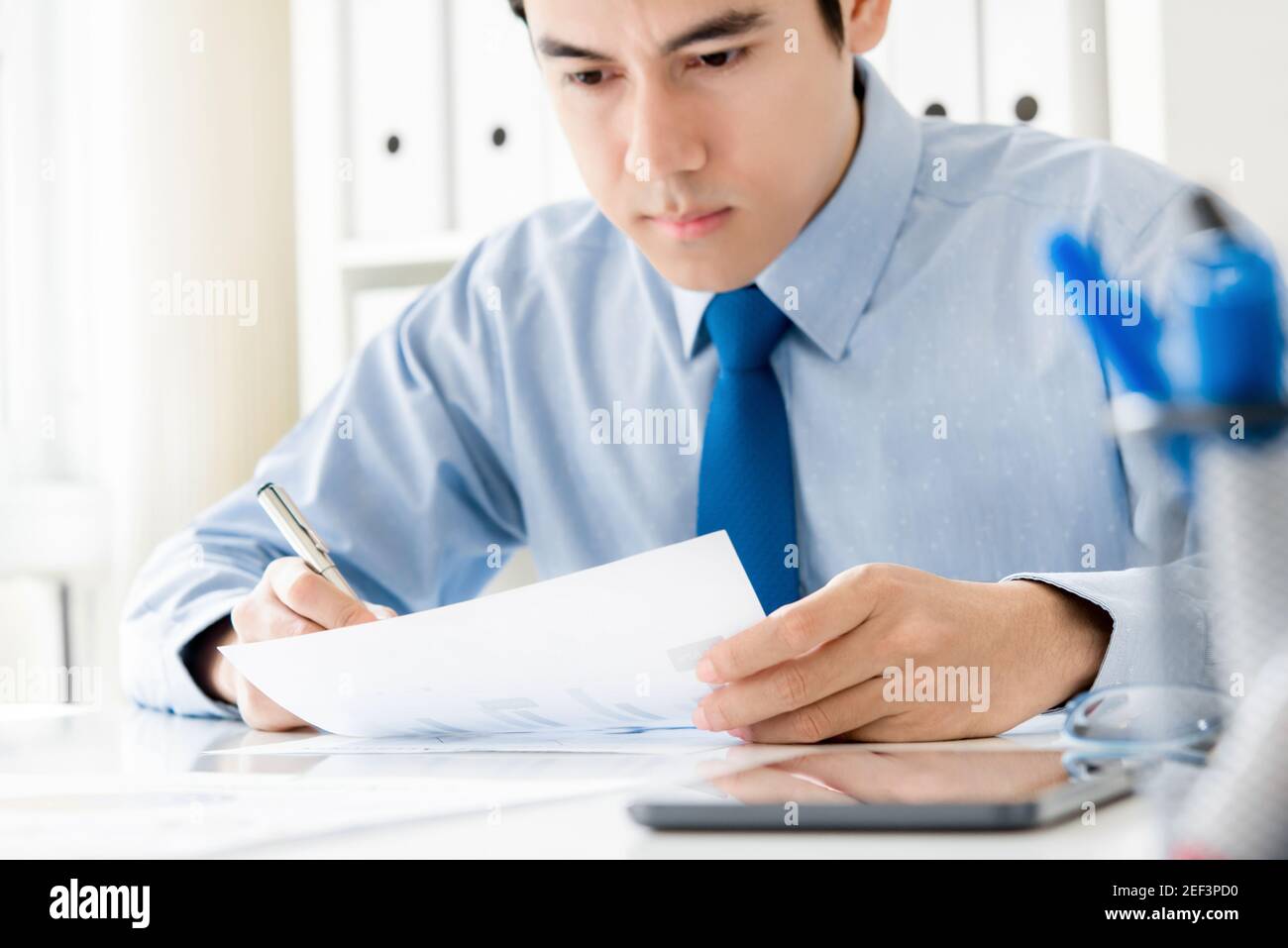 Giovane uomo d'affari che si concentra seriamente sulla documentazione in ufficio Foto Stock