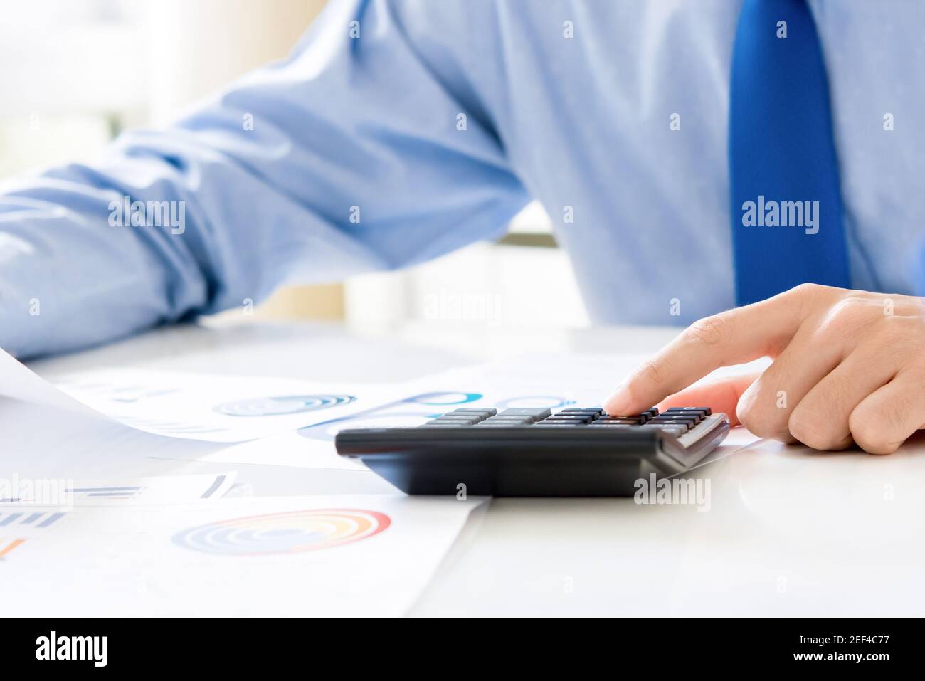 Calcolatore di pressione dell'uomo d'affari, calcolando e analizzando i dati finanziari alla scrivania Foto Stock