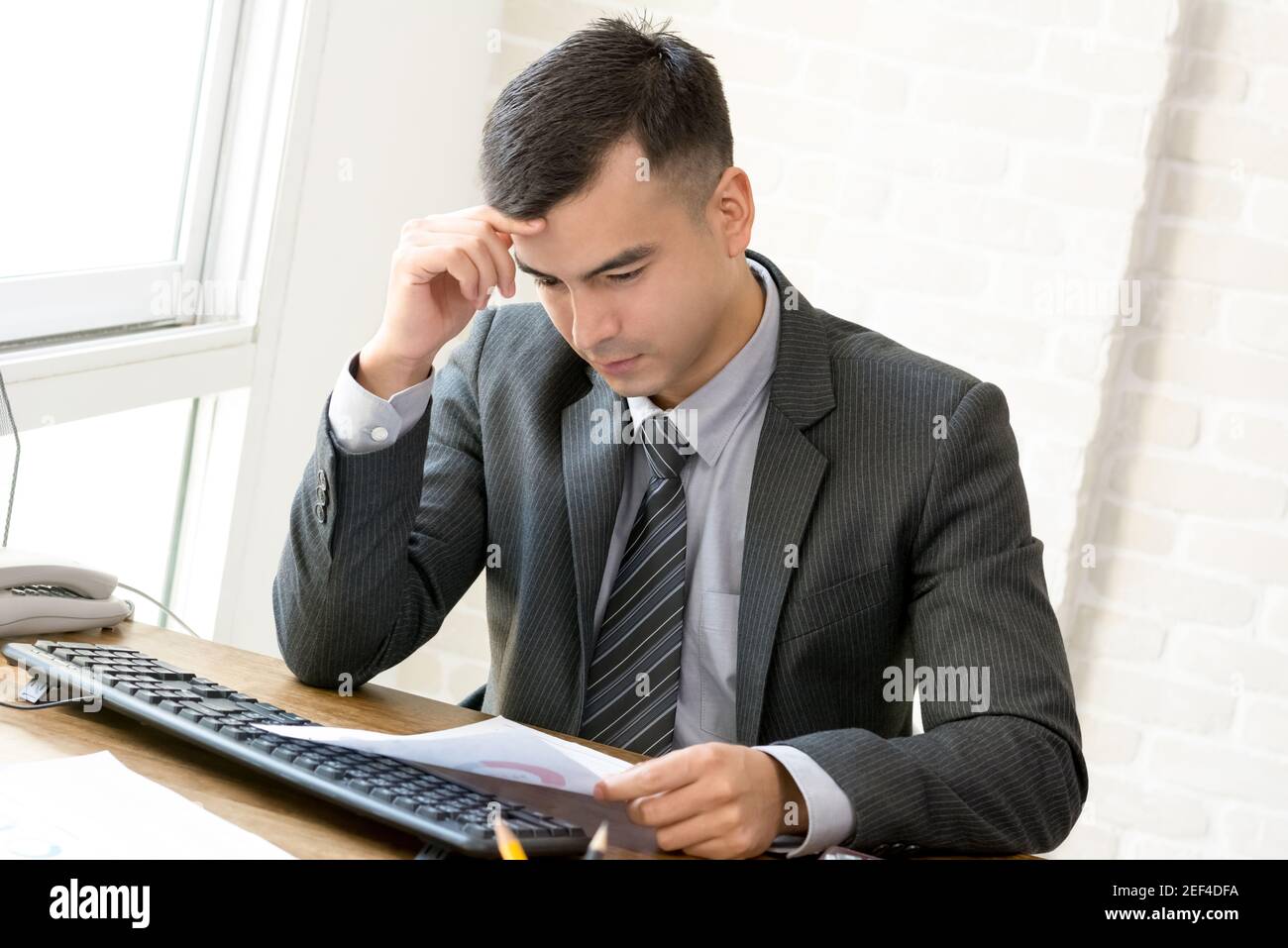 Uomo d'affari con la mano sul tempio che diventa serio durante la lettura del documento scrivania Foto Stock