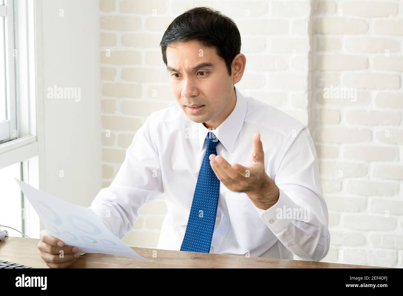 Uomo d'affari asiatico sempre sconvolto e deluso dopo aver letto il documento a. la sua scrivania Foto Stock