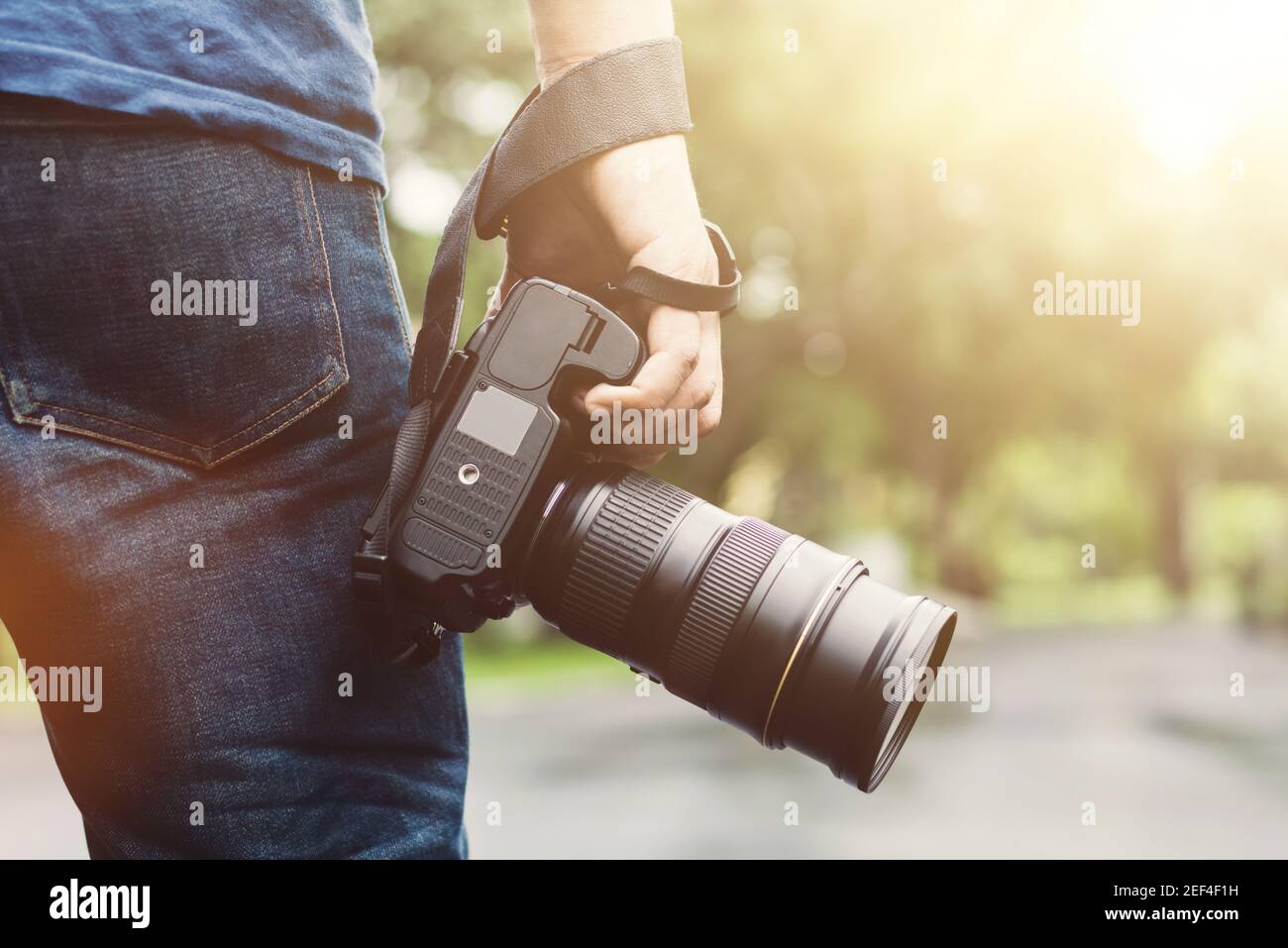 Mano del fotografo che tiene in mano la fotocamera DSLR mentre si cammina nel parcheggio Foto Stock