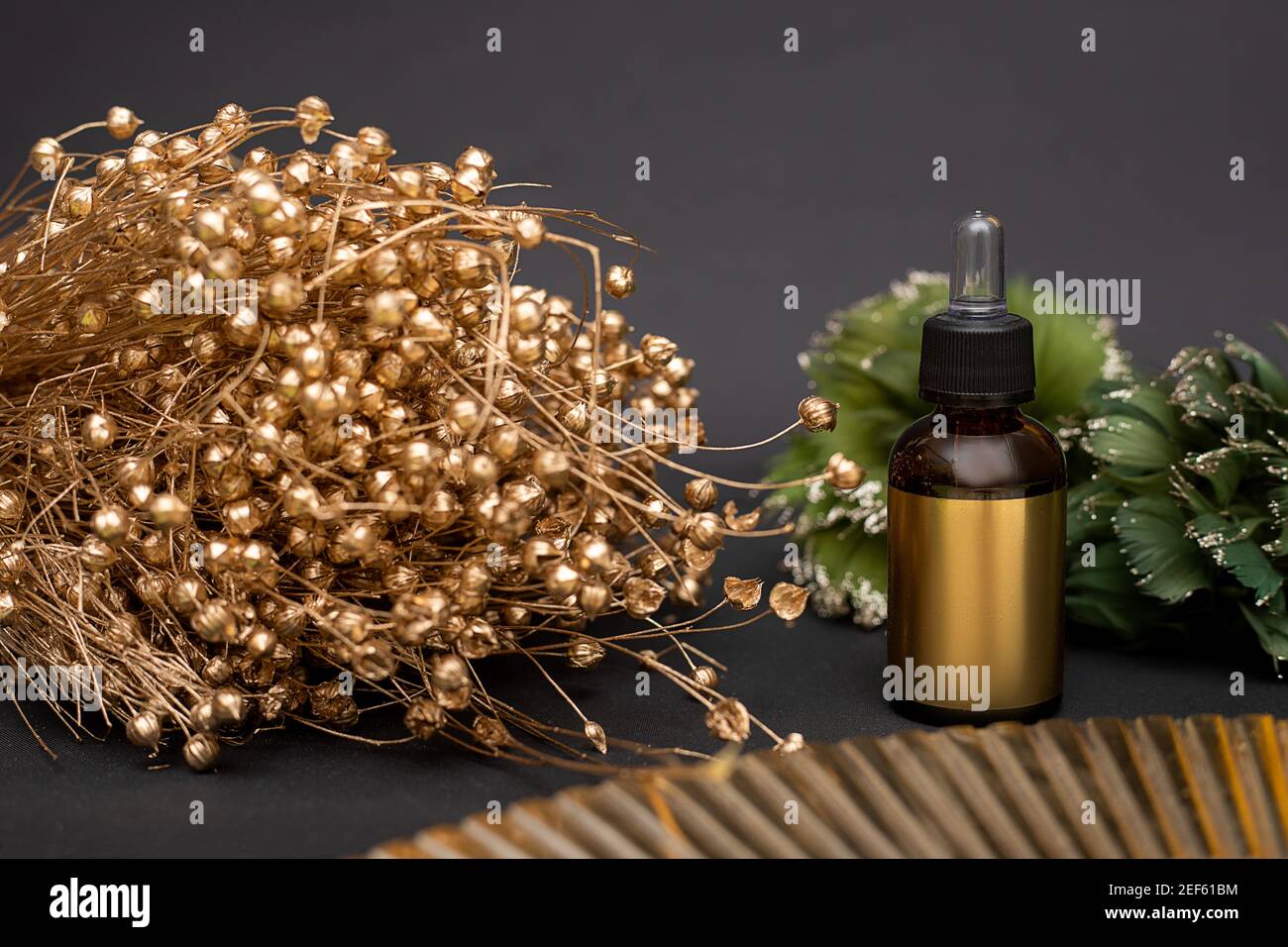 Bottiglia di vetro dorato con cosmetici su fondo nero con bouquet di fiori secchi dorati. Contagocce con olio cosmetico o siero. Viso anti-invecchiamento Foto Stock