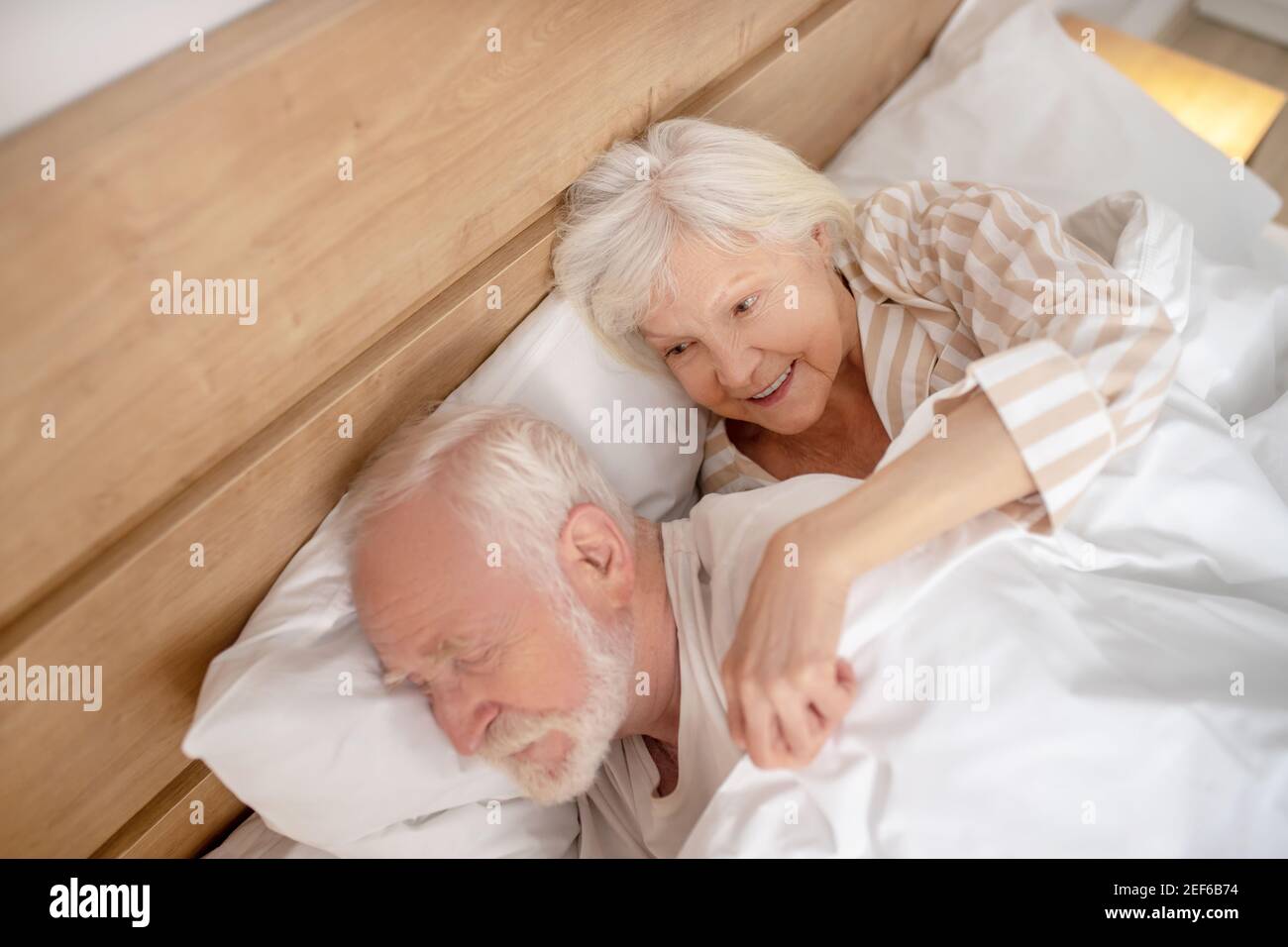Donna anziana dai capelli grigi che abbracciava il marito addormentato Foto Stock