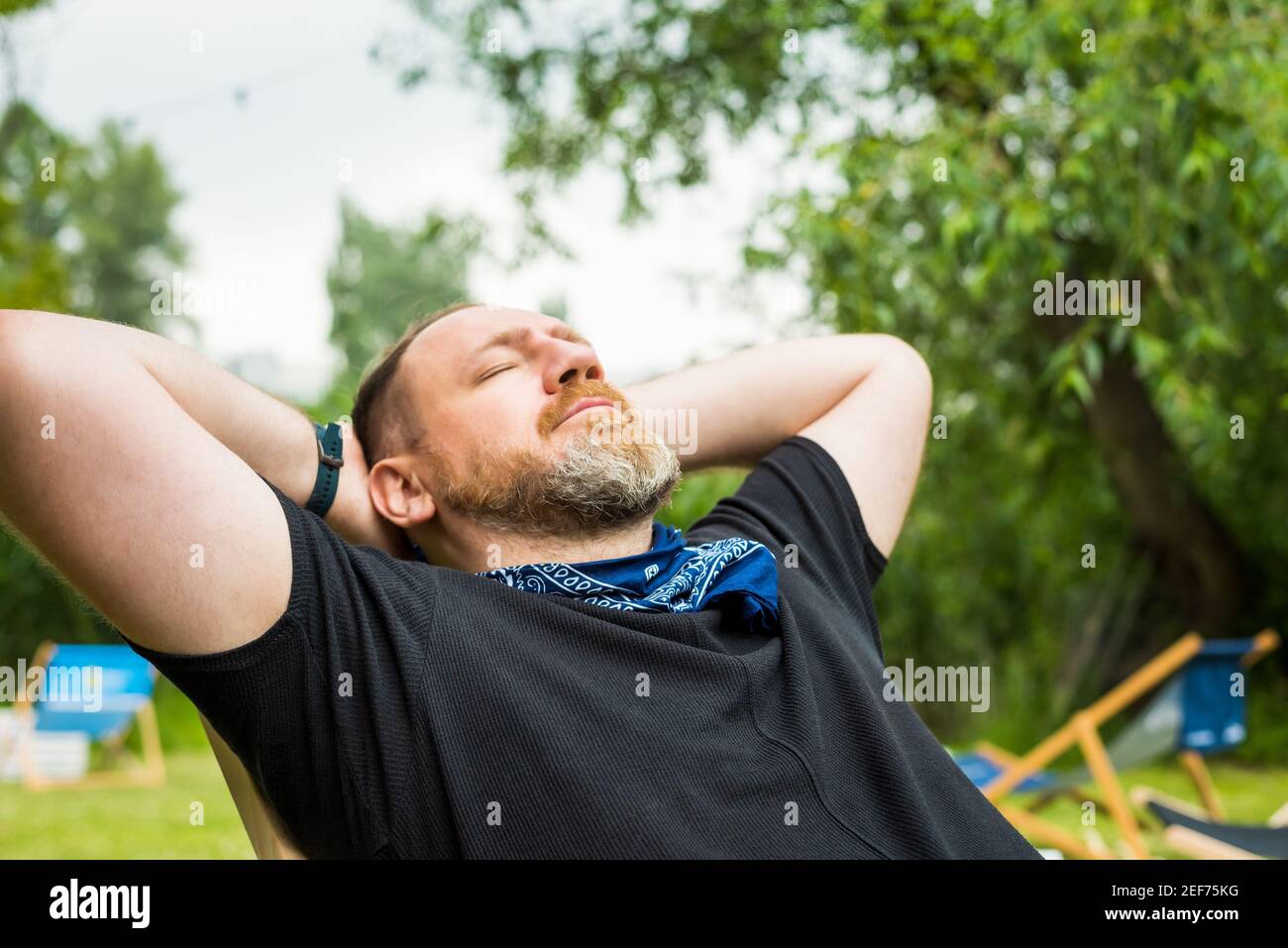 l'uomo adulto si rilassa all'aperto in un giardino sulla spiaggia della città che tiene le mani dietro la testa. solo attività all'aperto Foto Stock