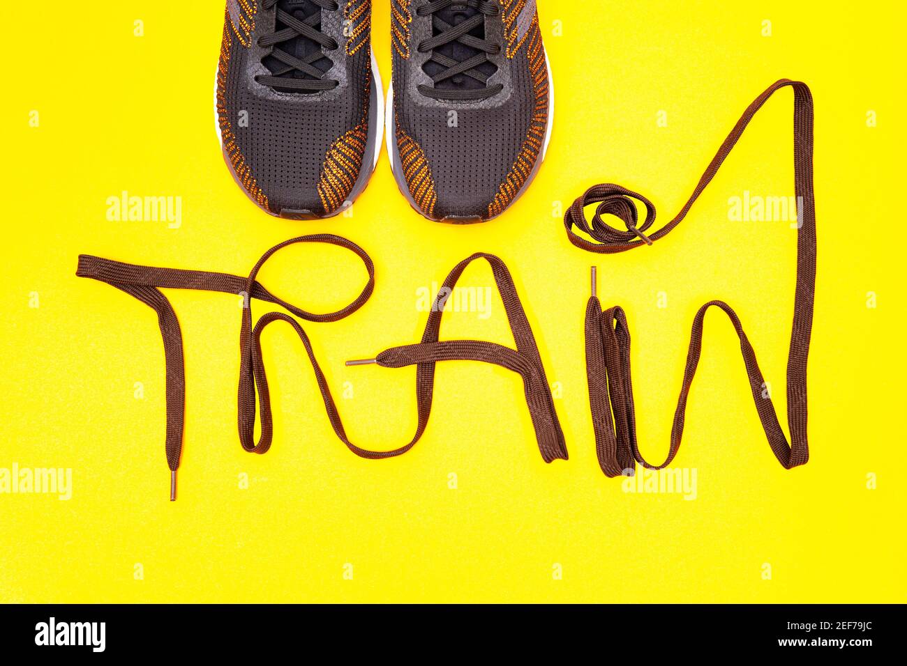 Un paio di sneaker atletiche nere e arancioni con scritta "Train" fatta di scarpe su sfondo giallo. Concetto di motivazione della formazione. Foto Stock