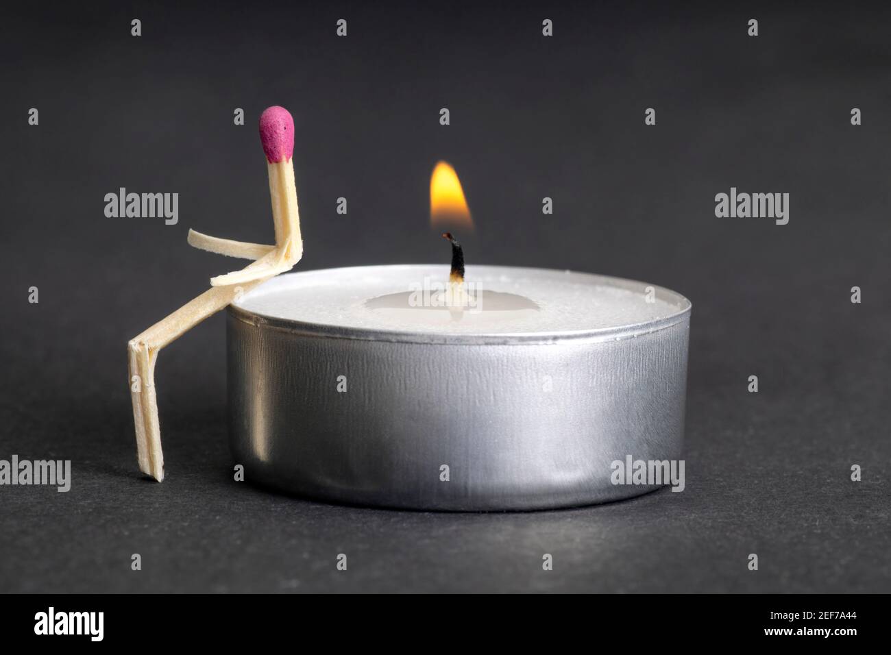 Personaggio matchstick seduto su una candela di tè illuminata. Concetto di solitudine e di amore senza richiesta. Foto Stock