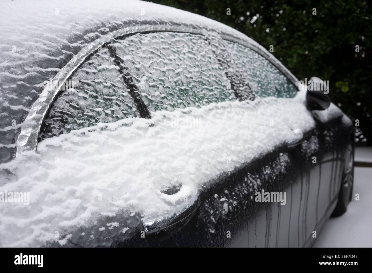 Chiusura della maniglia della porta congelata e dei finestrini di un'auto per le strade dopo una tempesta invernale di neve e pioggia gelida. Foto Stock