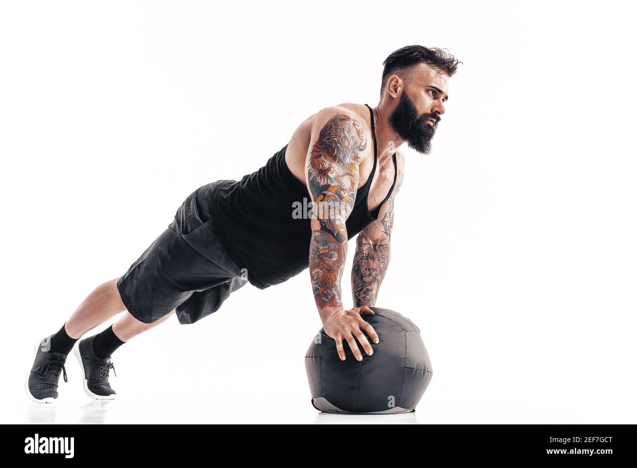 Muscolo tatuato sopportato maschio che esercita i pesi di idoneità Medicina Ball spinge gli esercizi in studio isolato su sfondo bianco. Foto Stock