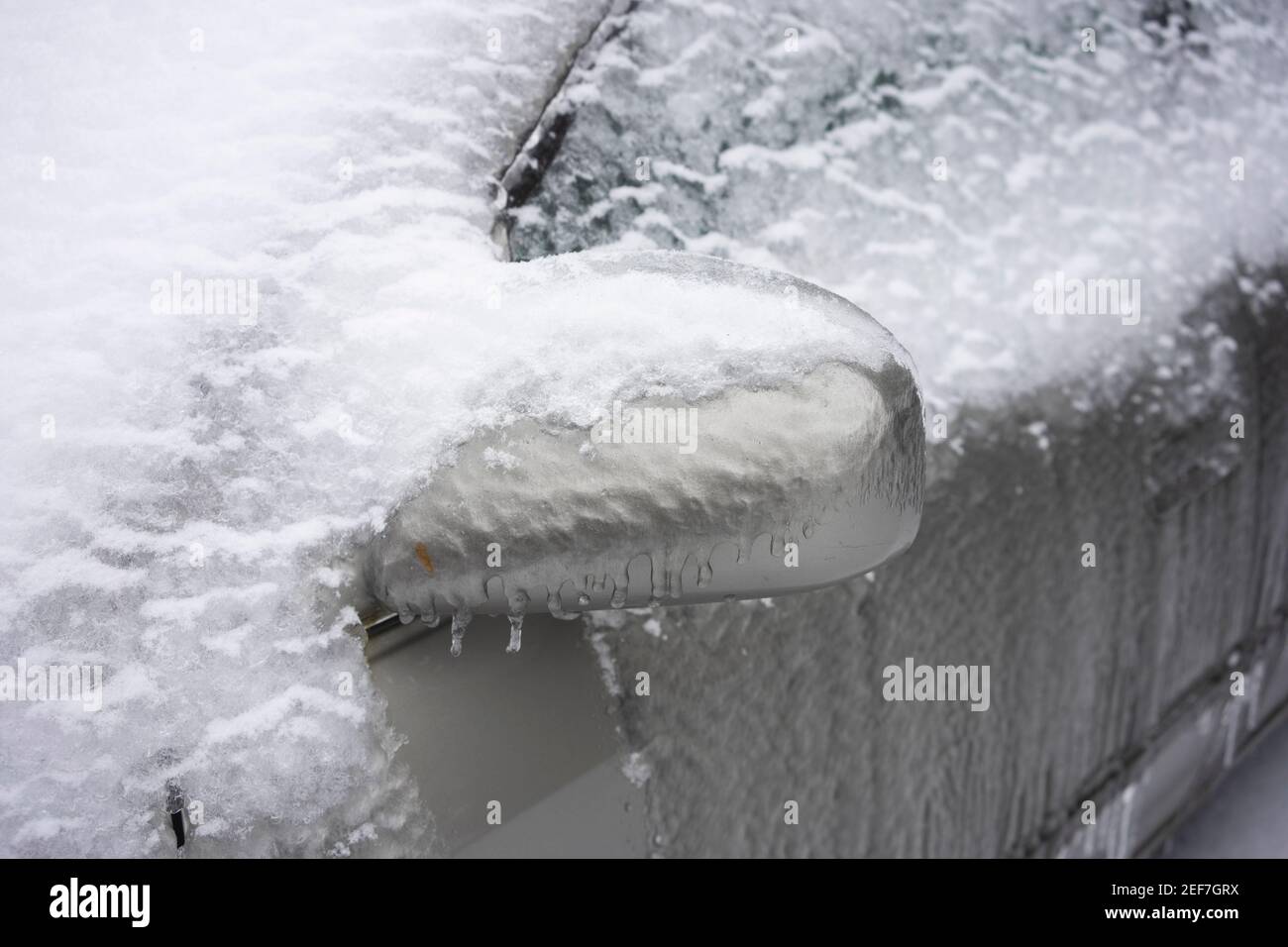 Primo piano dello specchio retrovisore ghiacciato una macchina dopo una tempesta invernale con neve e pioggia ghiacciata. Foto Stock