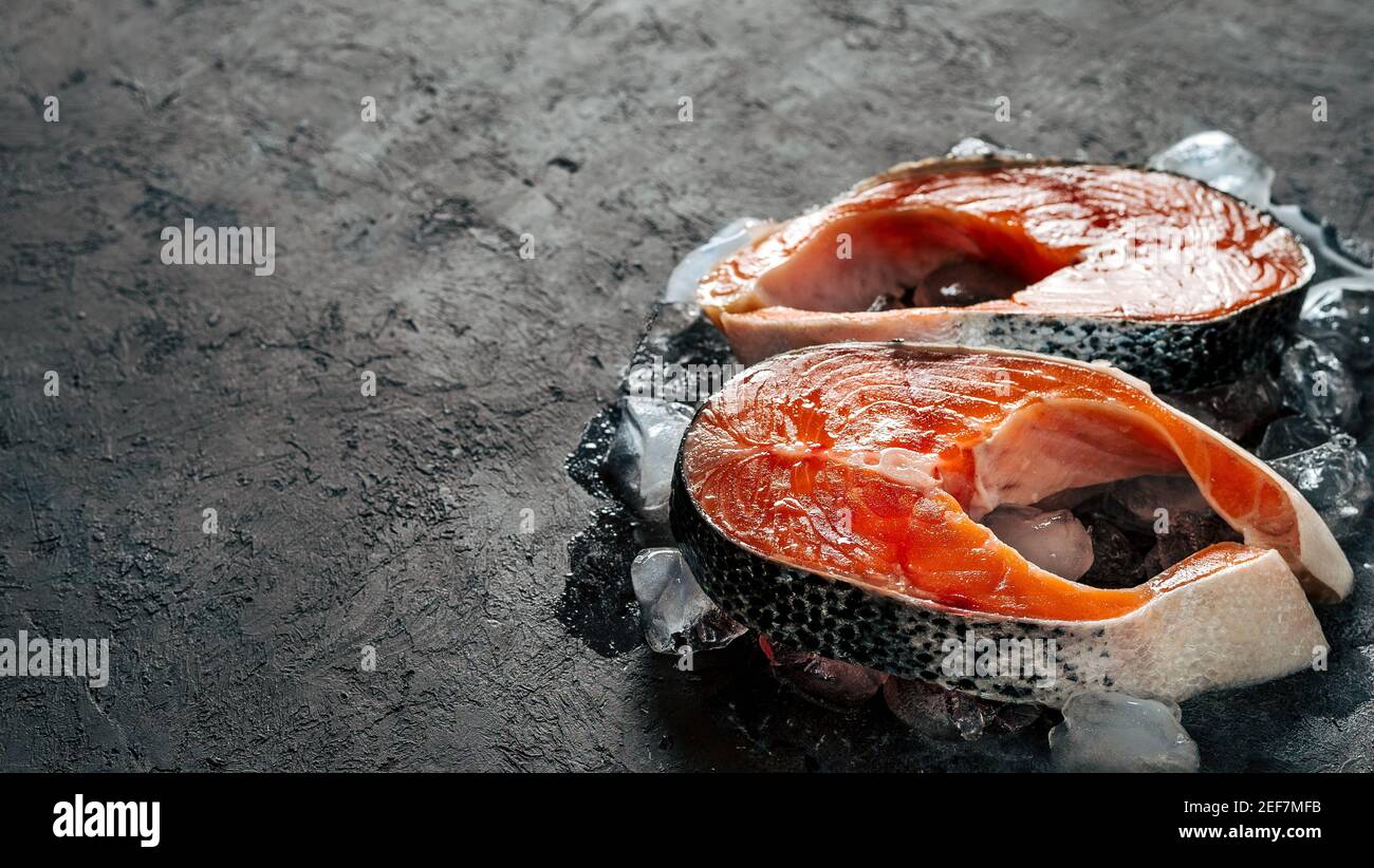 Due bistecche di salmone selvatico crudo su ghiaccio su sfondo nero testurizzato. Bistecche di salmone con spazio per la copia a sinistra. Banner orizzontale Foto Stock