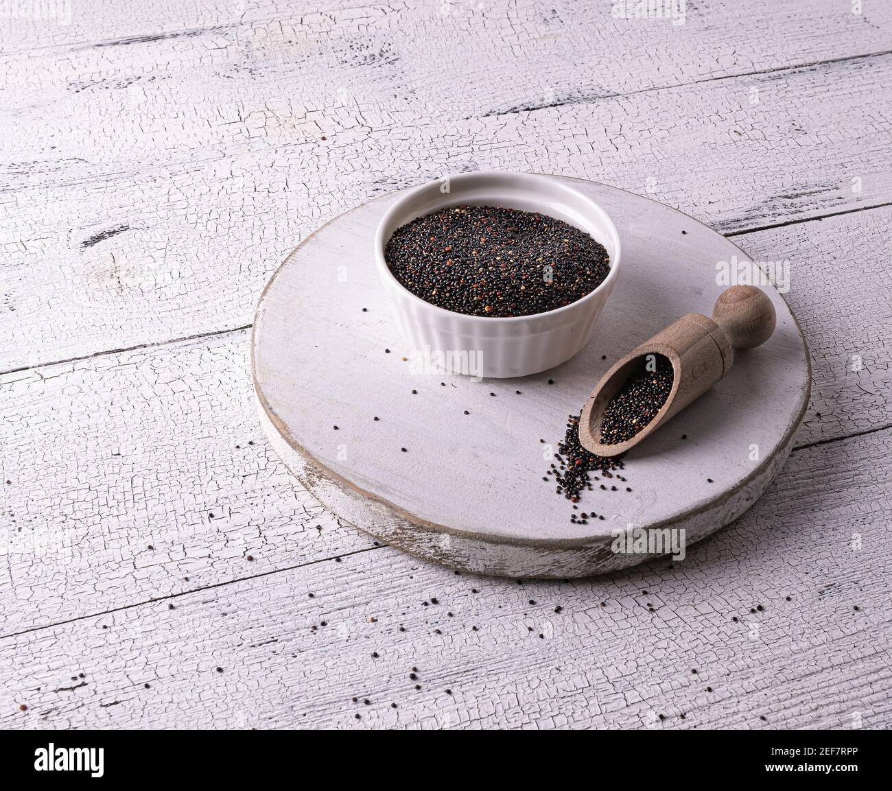 Semi crudi di quinoa nere non cotti in ciotola bianca e sccop a bordo e su tavolo di legno bianco. Pochi semi sono sparsi intorno. Cibo eccellente con spazio per la copia Foto Stock