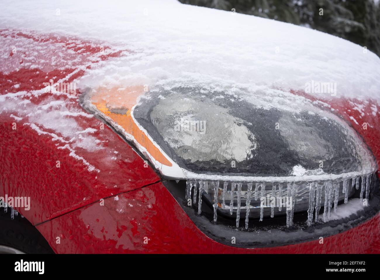Primo piano del faro di un'auto congelata per le strade dopo una tempesta invernale di neve e pioggia gelida. Foto Stock