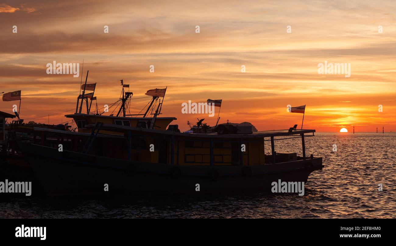 Sagome di barche da pesca con bandiere ormeggiate vicino KK Fish Mercato al tramonto Foto Stock