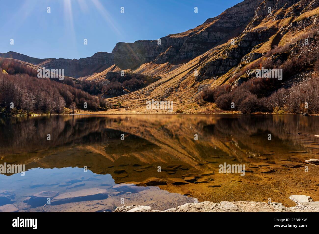 Il sole sul Lago di Baccio mentre le montagne appenniniche si riflettono nell'acqua, Pievepelago, Italia Foto Stock