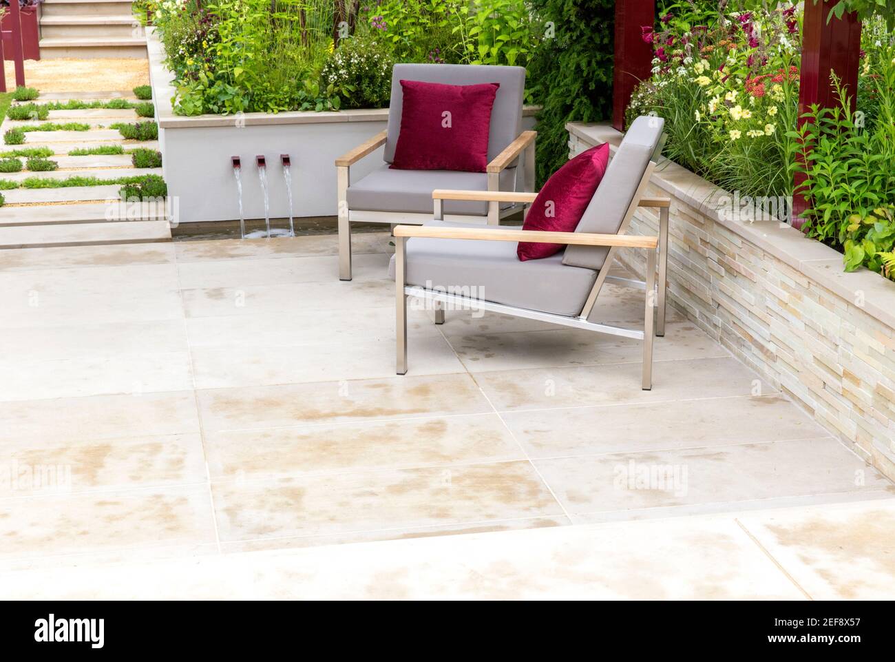 Moderno patio con giardino in pietra urbana e sedie con mobili da giardino Cuscini rossi - bordi del giardino del letto rialzato - Estate - Londra UK Inghilterra Foto Stock