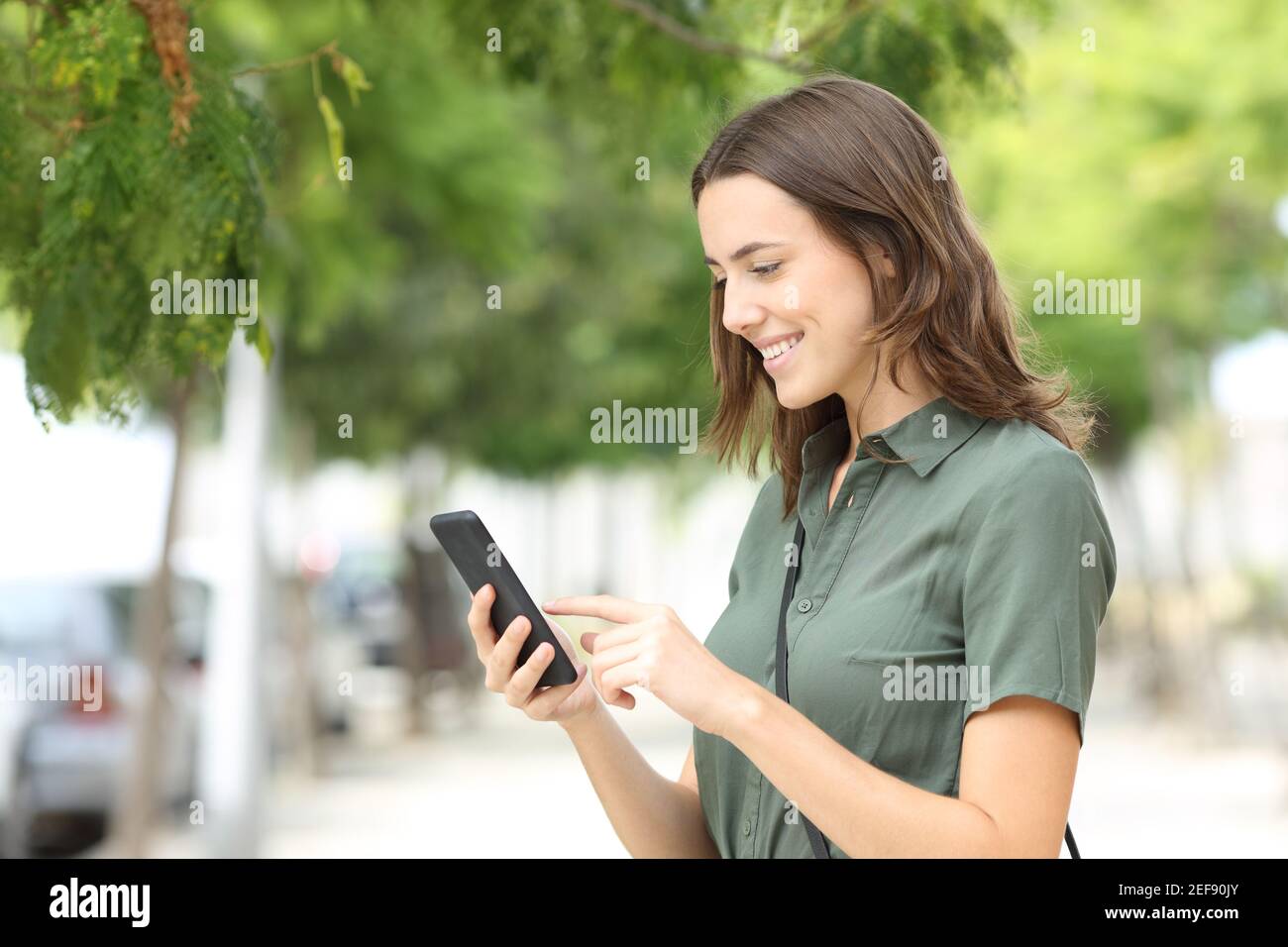 Donna felice che cammina usando lo smartphone in una strada della città Foto Stock