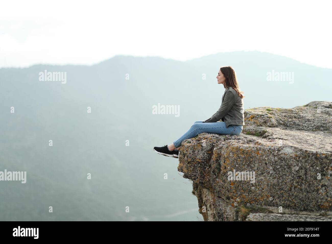 Profilo del corpo pieno di una donna penosa seduta contemplando le viste sulla cima di una scogliera in montagna Foto Stock