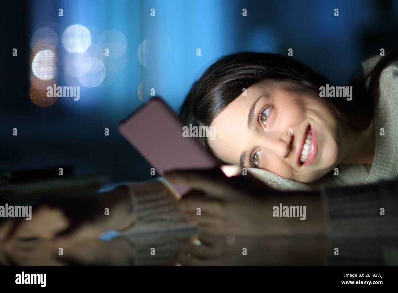 Donna felice in tarda notte controllare smartphone contenuti a casa Foto Stock