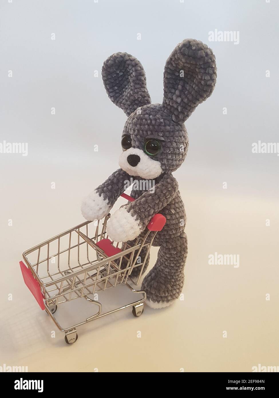 Primo piano di peluche a crocheted coniglietto con carrello vuoto giocattolo su sfondo bianco. Foto Stock