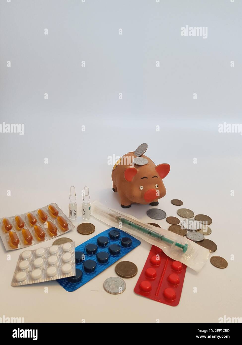 Banca piggy con soldi, pillole, farmaci, siringhe, ampolle su sfondo bianco. Costi di trattamento. Guadagni sui farmaci. Foto Stock