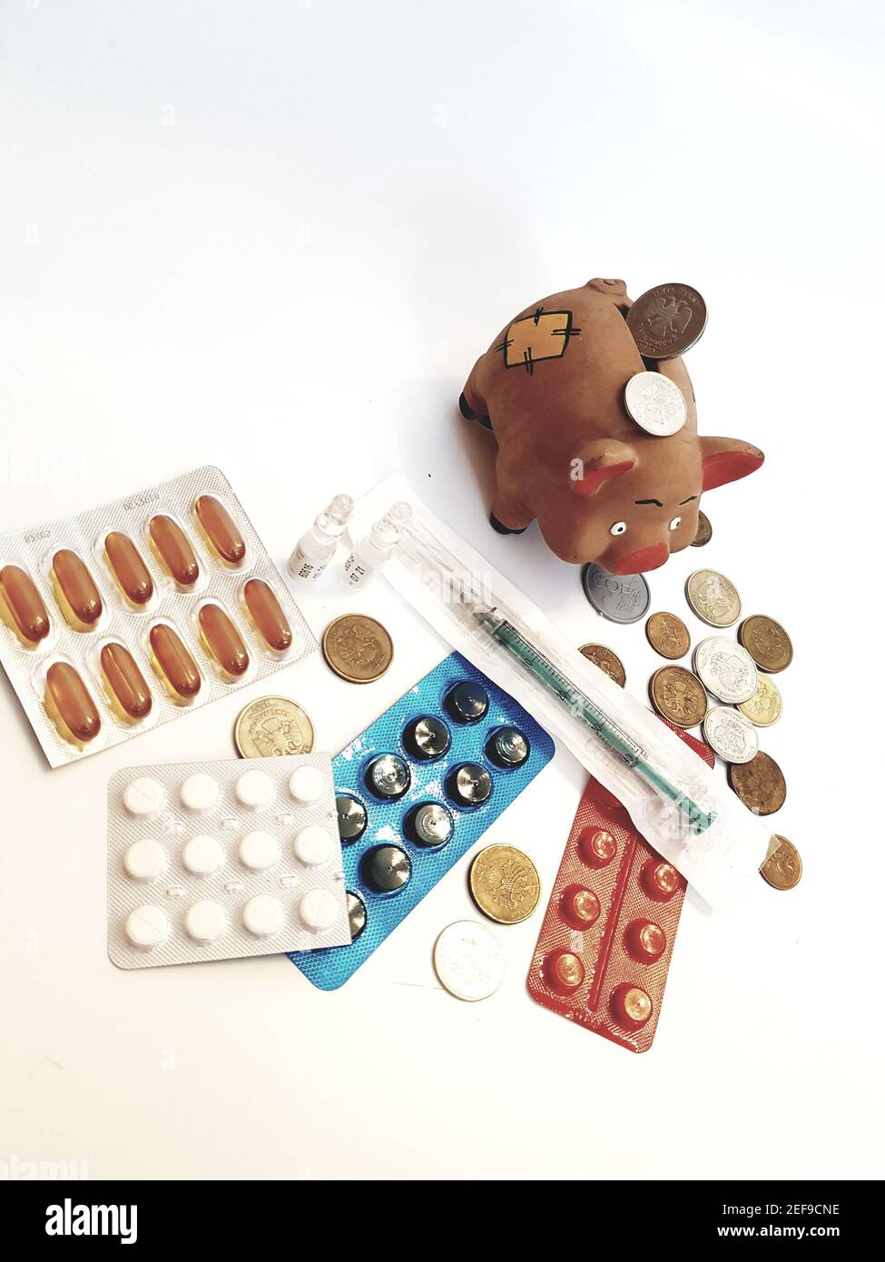Banca piggy con soldi, pillole, farmaci, siringhe, ampolle su sfondo bianco. Costi di trattamento. Guadagni sui farmaci. Foto Stock