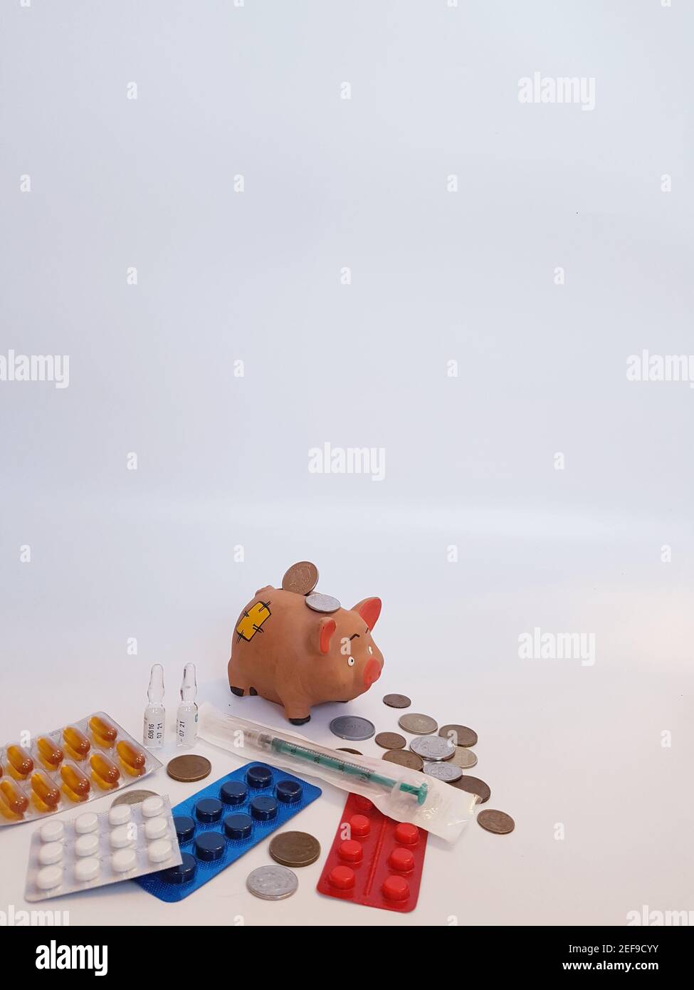 Banca piggy con soldi, pillole, farmaci, siringhe, ampolle su sfondo bianco. Costi di trattamento. Guadagni sui farmaci. Foto Stock