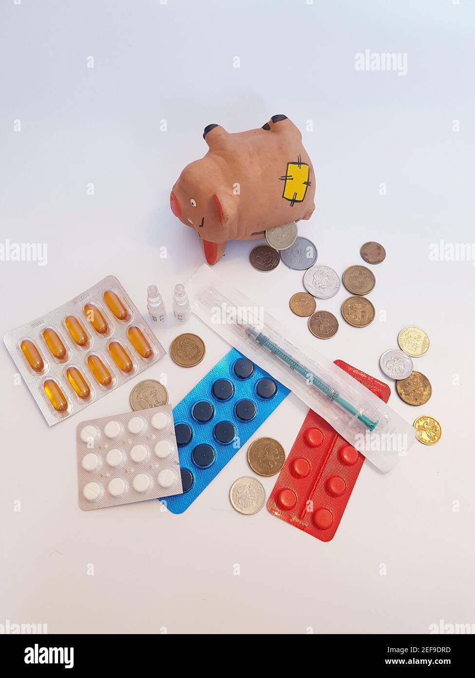 Banca piggy con soldi, pillole, farmaci, siringhe, ampolle su sfondo bianco. Costi di trattamento. Foto Stock