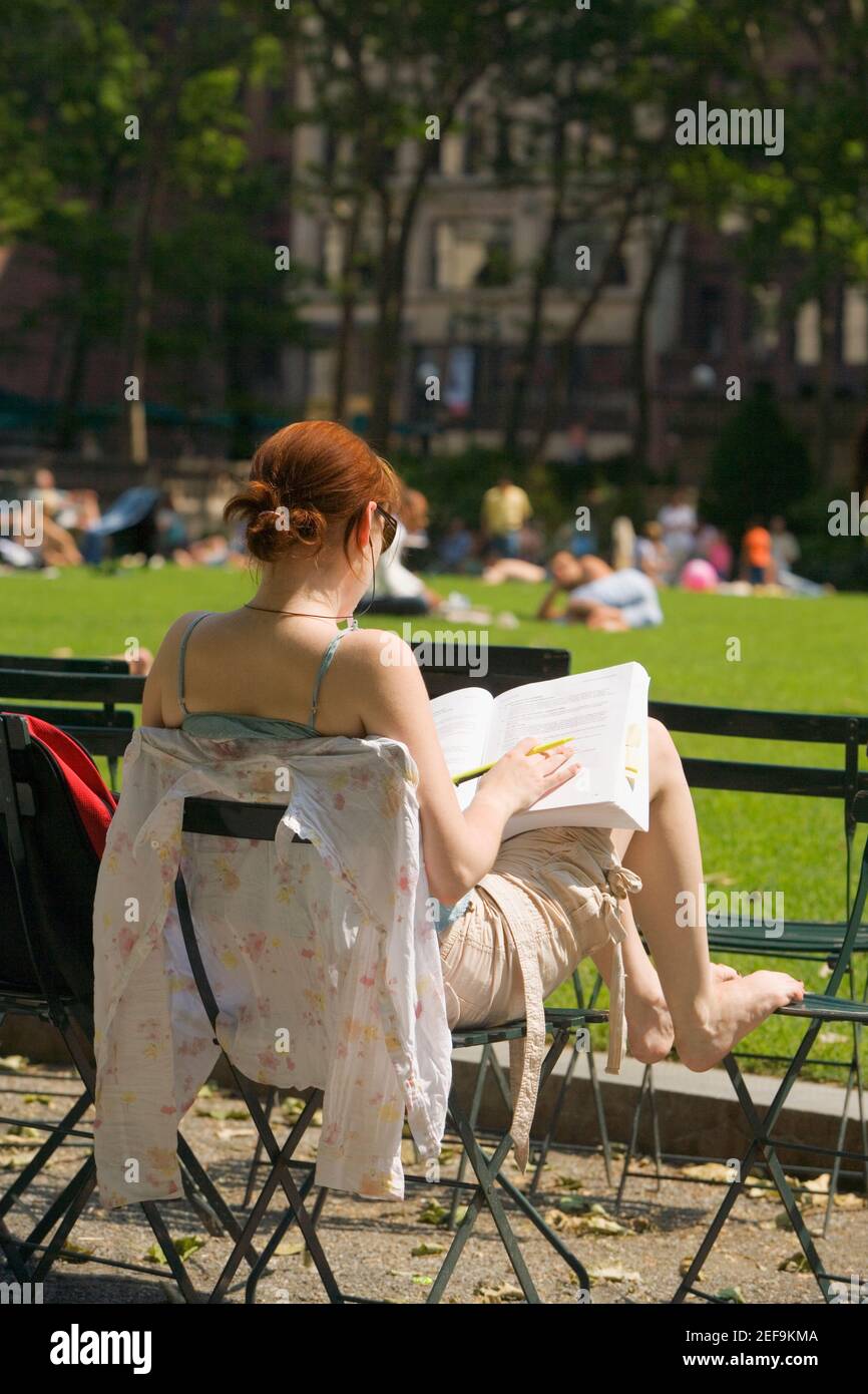 Vista posteriore di una donna seduta su una sedia e. leggere un libro Foto Stock