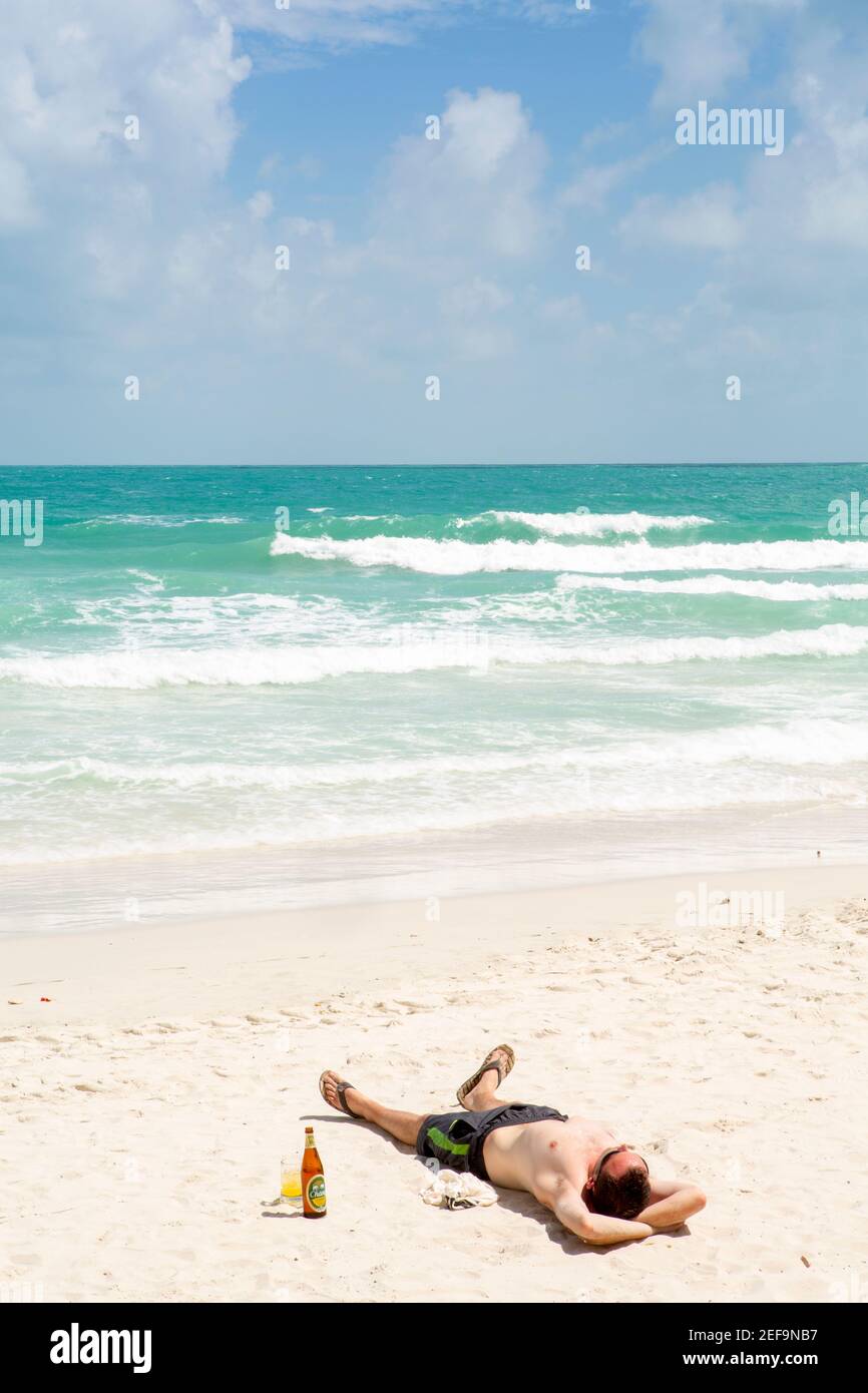 Uno zaino in spalla scottato al sole che dorme sulla spiaggia con birra ghiacciata, Haad Rin (aka Sunrise) festa spiaggia & luogo della festa della Luna piena, Ko Phangan, Thailandia Foto Stock