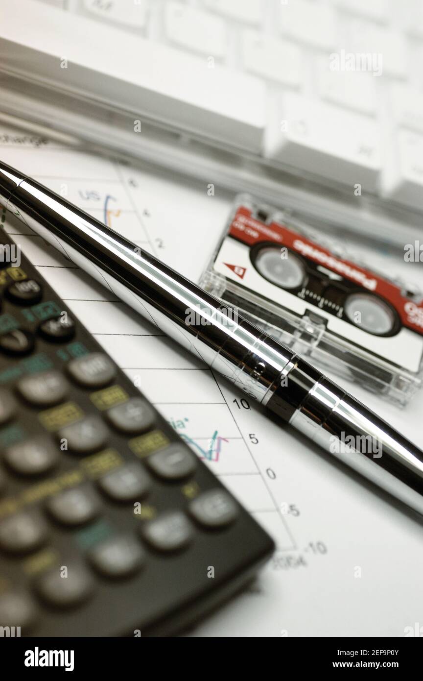 Calcolatrice, tastiera per computer, cassetta di registrazione micro e penna in cima al grafico finanziario, primo piano Foto Stock