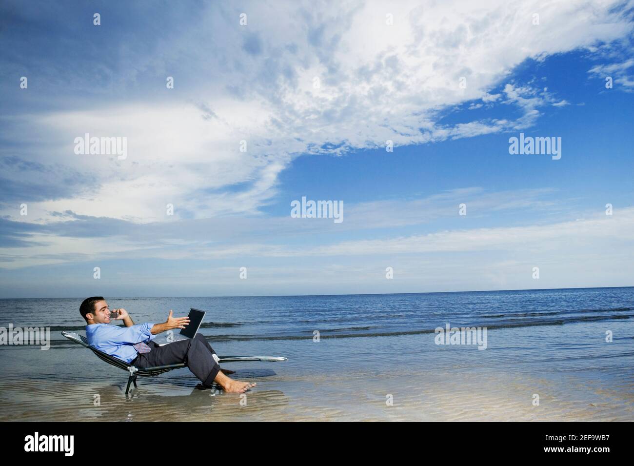 Profilo laterale di un giovane seduto sulla spiaggia con un computer portatile Foto Stock