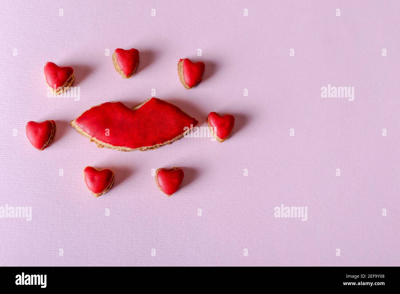 Biscotti a forma di labbra e piccoli cuori intorno isolati su sfondo viola con spazio di copia per testo o disegno. San Valentino e romantico Foto Stock