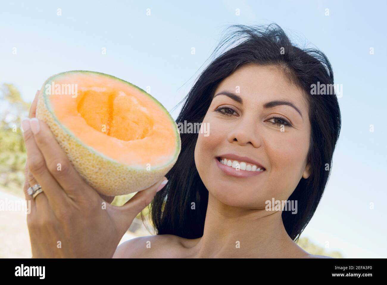 Ritratto di una donna mid adulta che tiene un mezzo melone e sorridendo Foto Stock