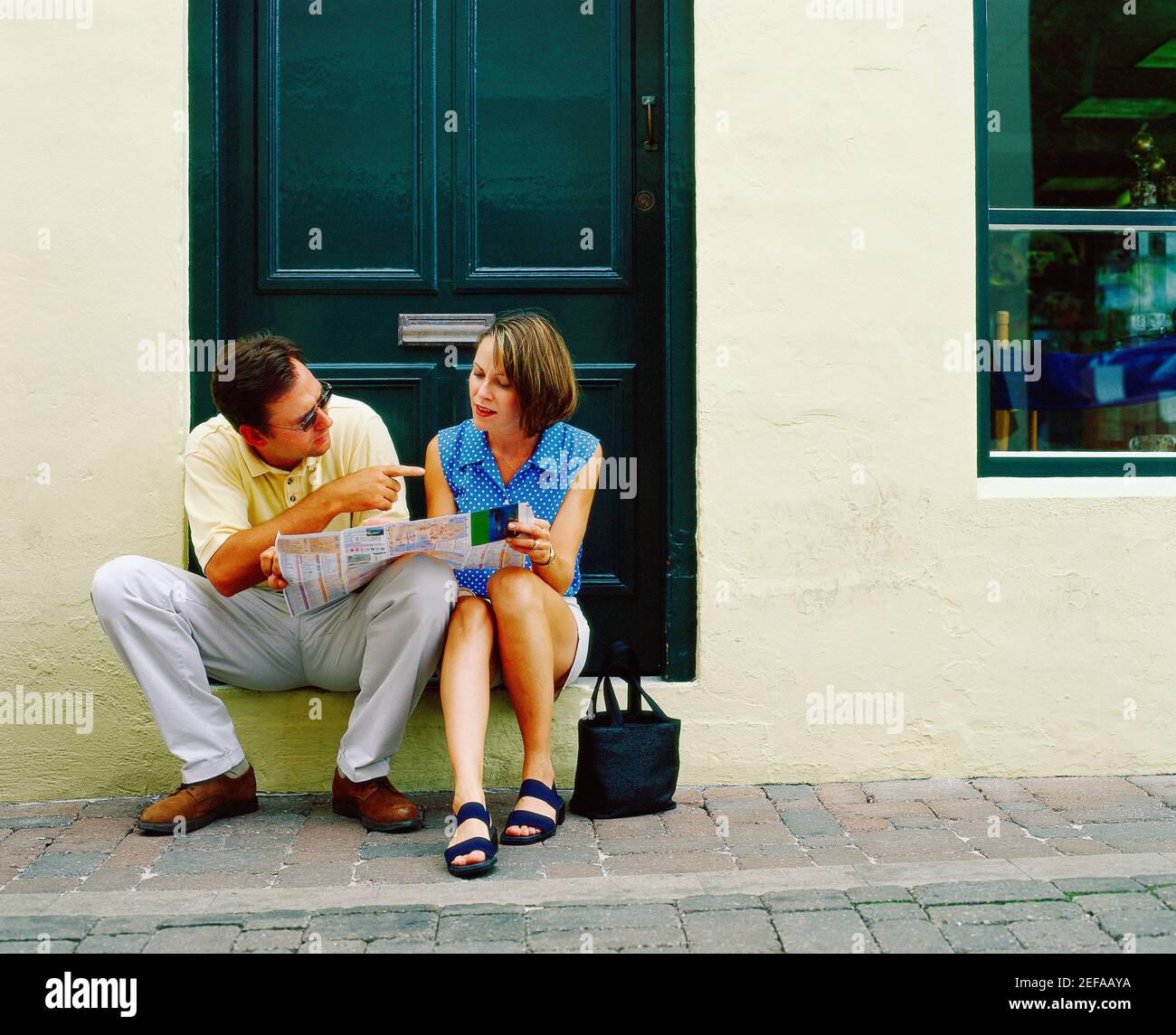 Giovane coppia seduta di fronte ad una porta e tenendo un giornale, Bermuda Foto Stock