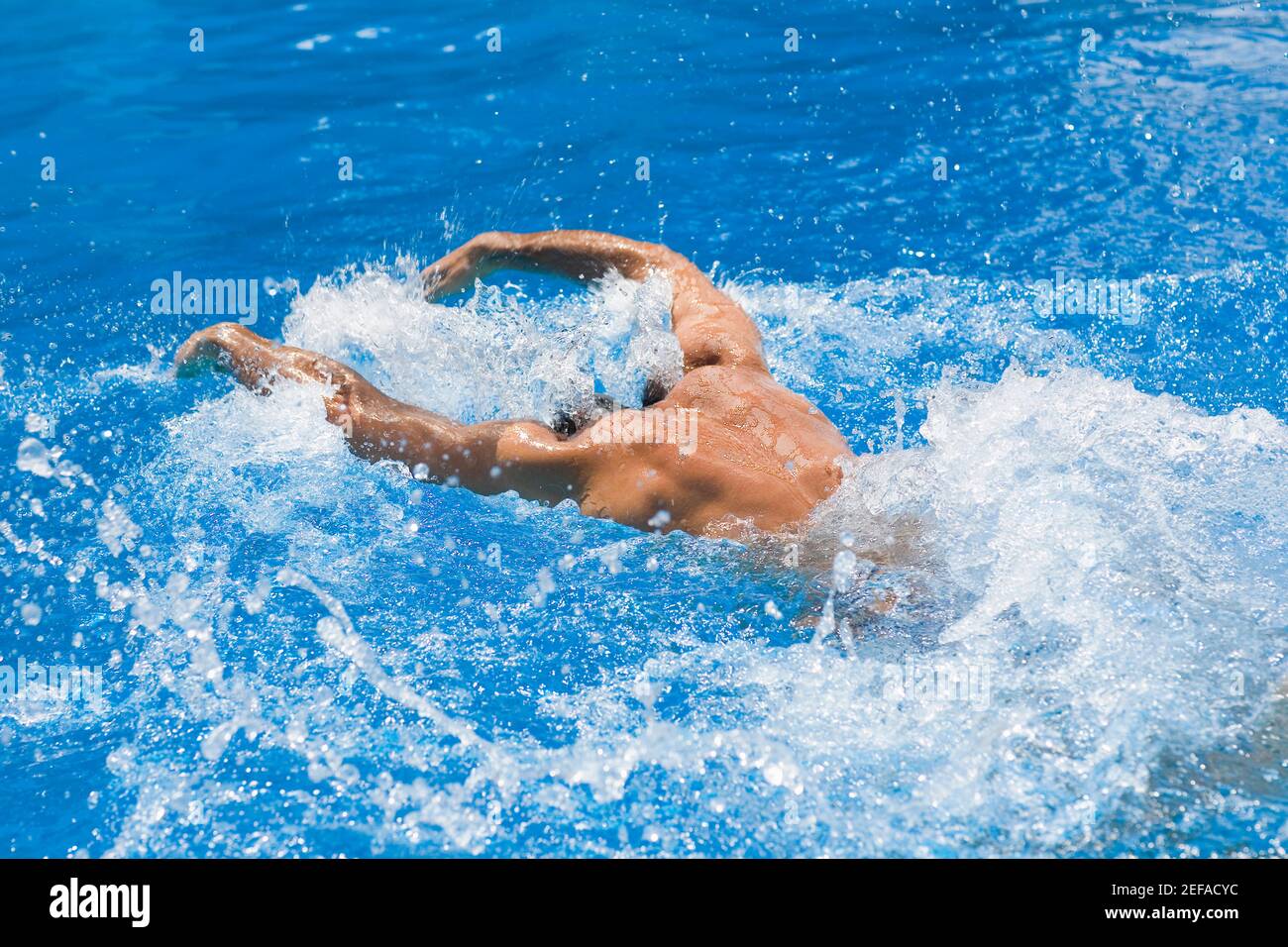 Vista posteriore di un uomo che nuota la corsa della farfalla dentro una piscina Foto Stock