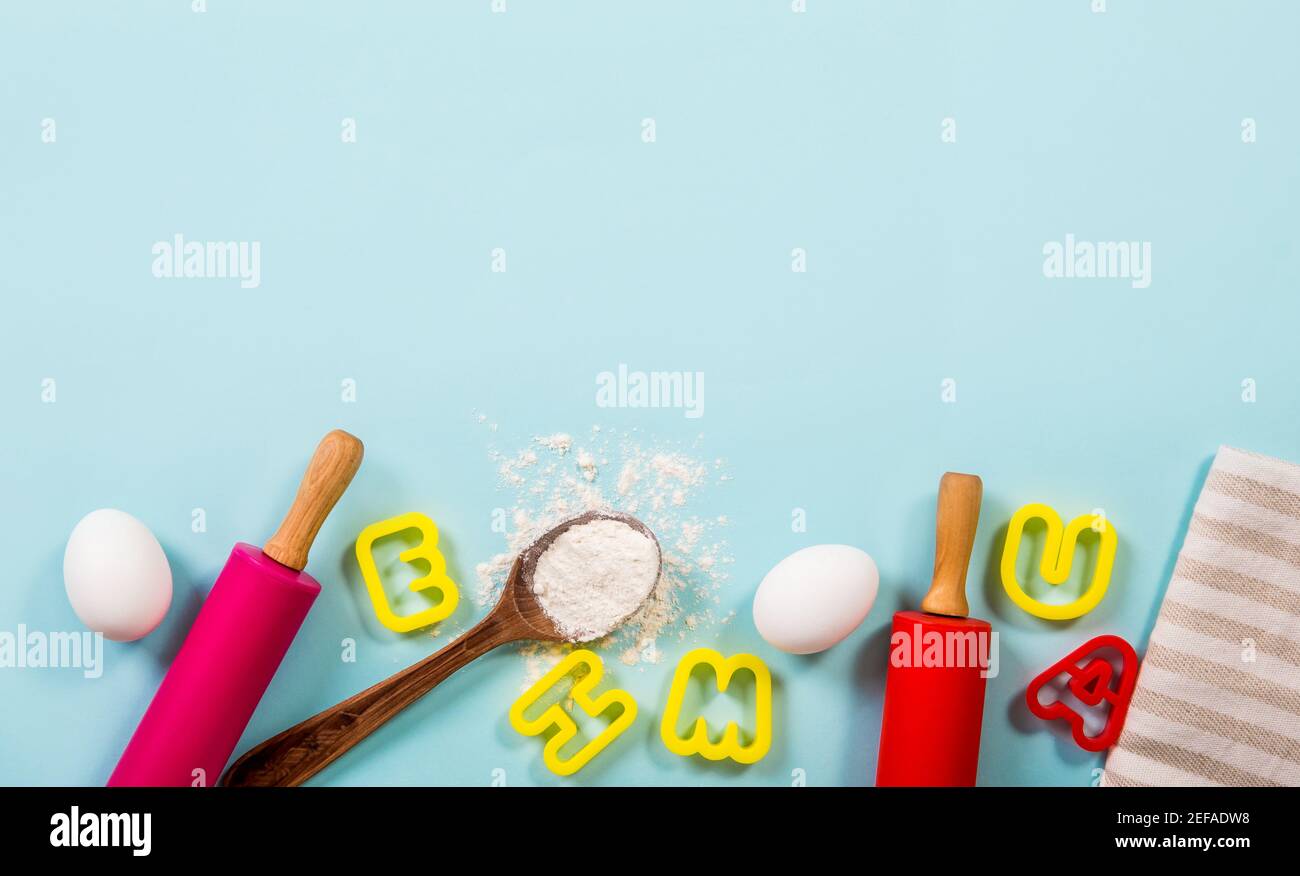 Divertente lezione di cucina per bambini concetto di bordo lotto di spazio per il testo. Uova, farina, spille, frese per biscotti a forma di lettera su fondo azzurro. Foto Stock
