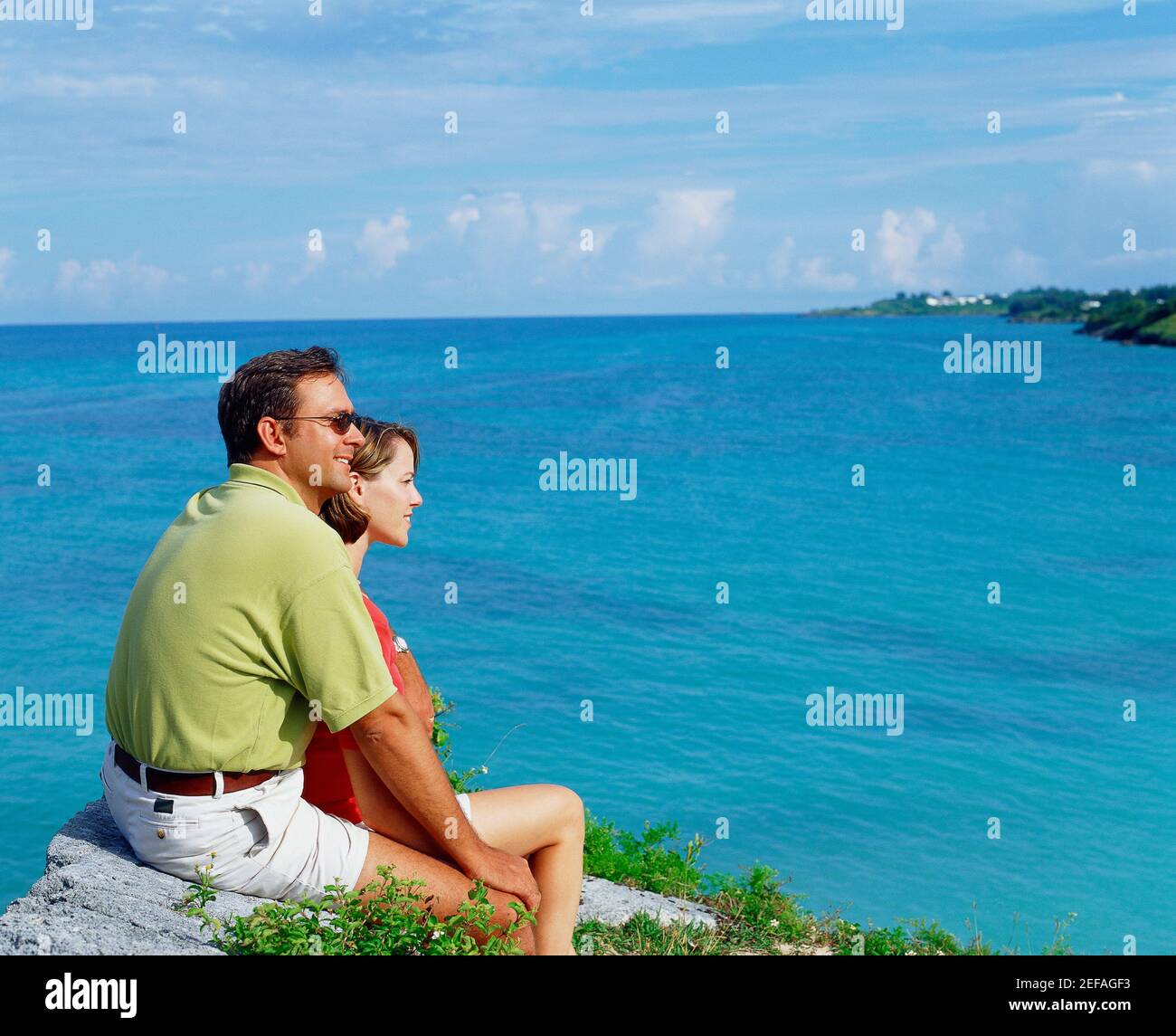 Profilo laterale di una giovane coppia seduta insieme su una roccia, Bermuda Foto Stock