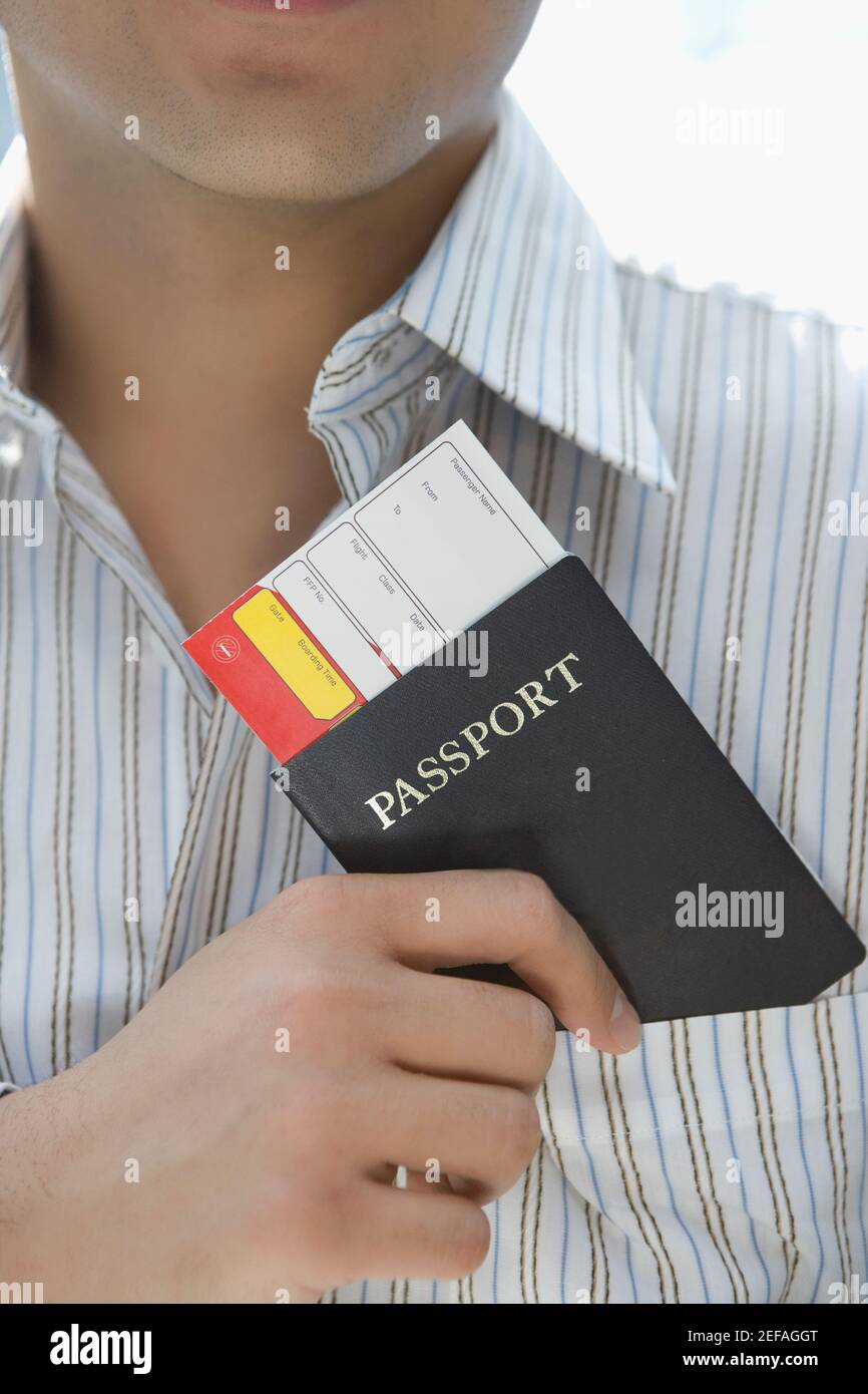 Vista in sezione intermedia di un giovane uomo che mette un passaporto Con un biglietto aereo in tasca shirtÅ½s Foto Stock