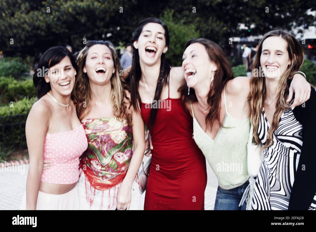Cinque giovani donne che si levano in piedi con le braccia l'una intorno all'altra e ridendo Foto Stock