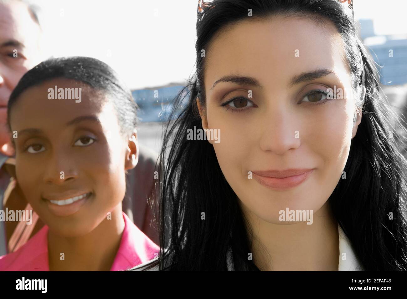 Primo piano di due donne d'affari che sorridono con un uomo d'affari alle loro spalle Foto Stock