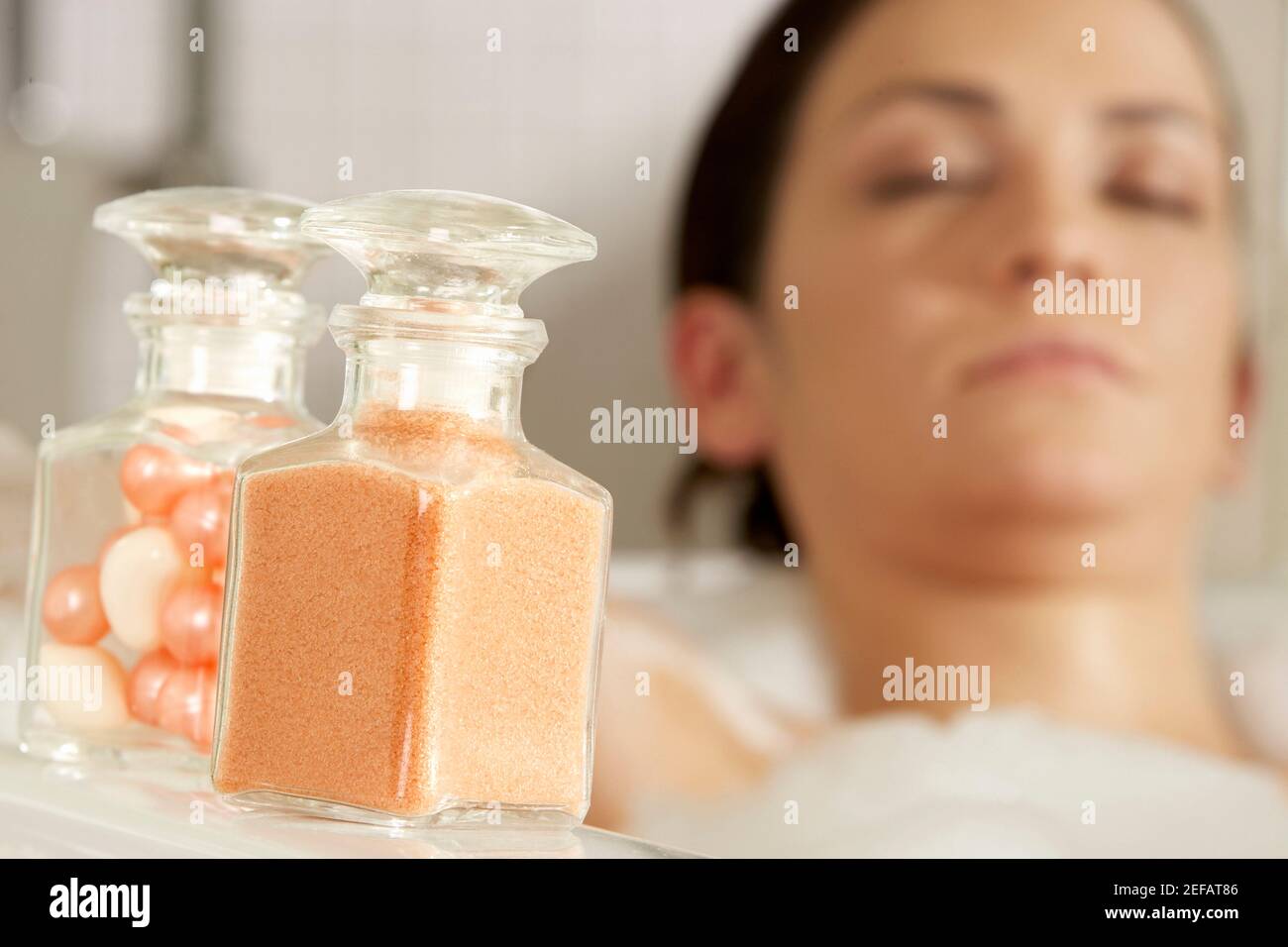 Primo piano di una polvere da bagno e perle da bagno in vetro bottiglie con una giovane donna nella vasca da bagno nella sfondo Foto Stock