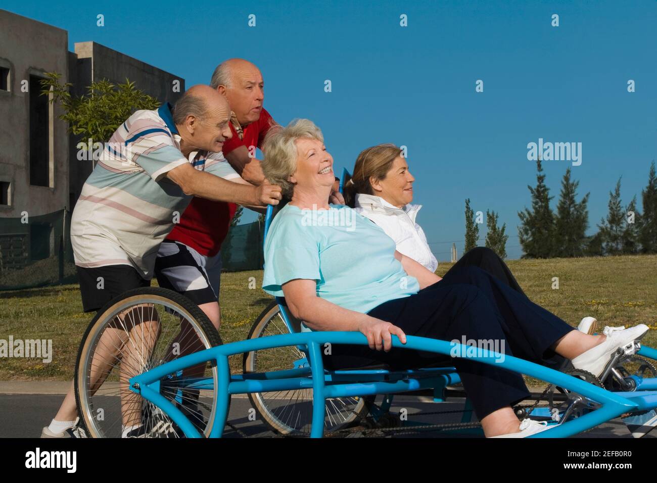 Due donne anziane che siedono su un quadriciclo e due senior uomini che lo spingono Foto Stock