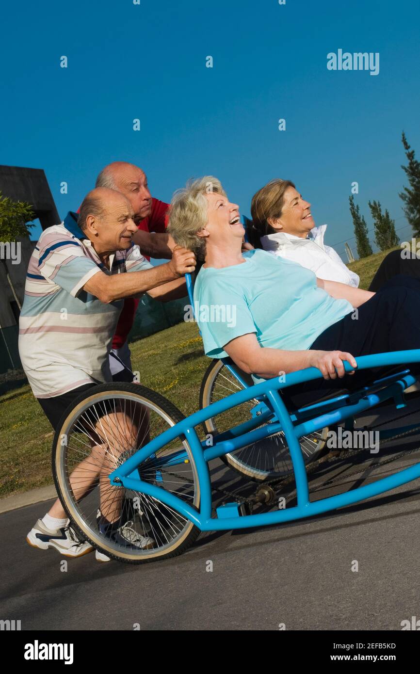 Due donne anziane che siedono su un quadriciclo e due senior uomini che lo spingono Foto Stock