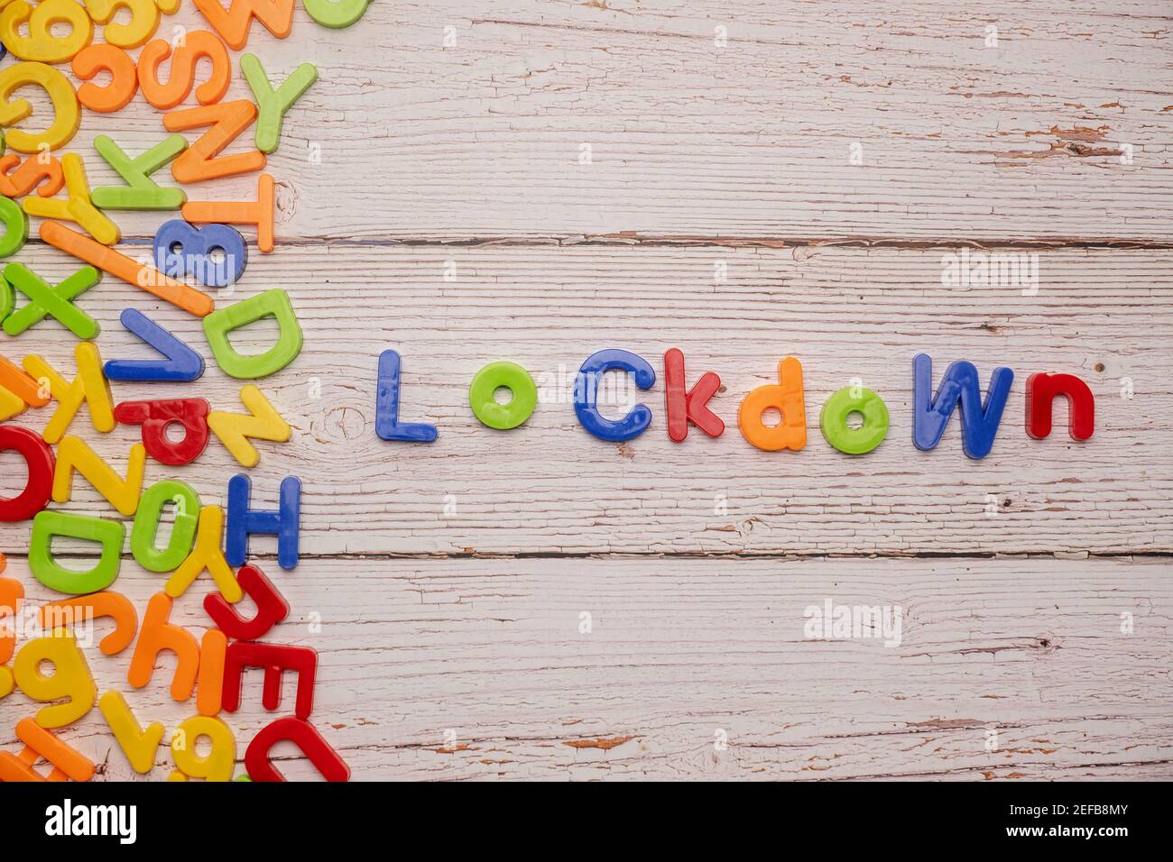 Lettere magnetiche colorate su un tavolo bianco rustico durante la casa Incoronavirus scolastico che scrive fuori LOCKDOWN Foto Stock